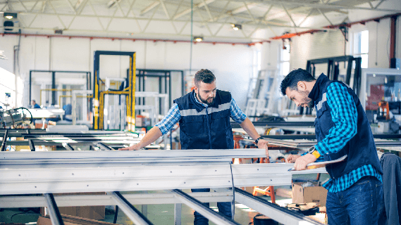 Two fabricators checking a frame against a printed specification on a manufacturing floor.
