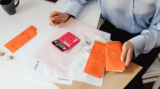 Receipts, a pink calculator and paperwork spread across a desk.